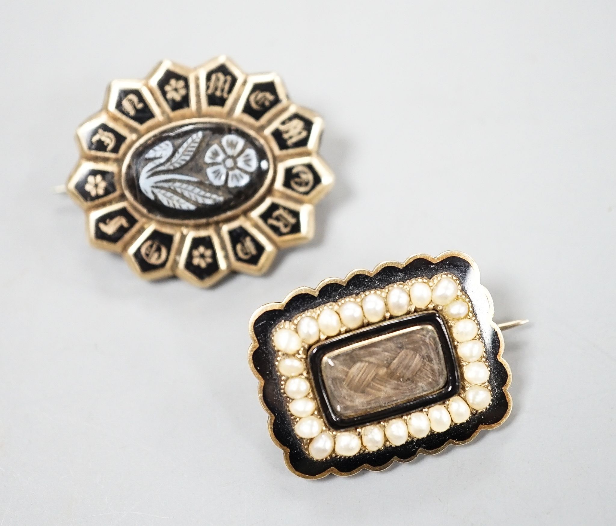 Two 19th century yellwo metal mourning brooches, one with plaited hair, split pearls and engraved inscripotion, the other with sardonyx centre stone, largest 27mm.